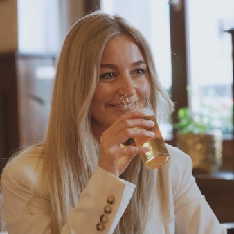 Eine Frau mit blonden Haaren hat ein Kölsch in der Hand und lacht ihr Gegenüber an.