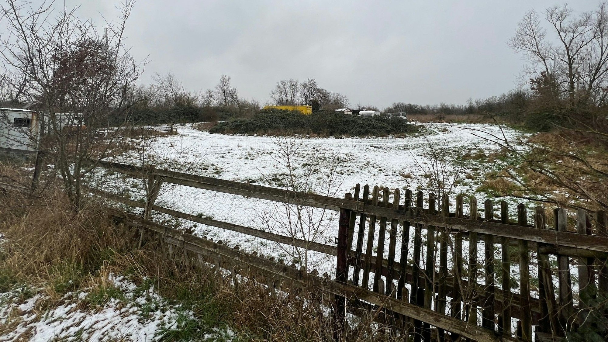 Ein mit Holzzaun umzäunte Wiese mit geparkten Fahrzeugen in der Mitte.