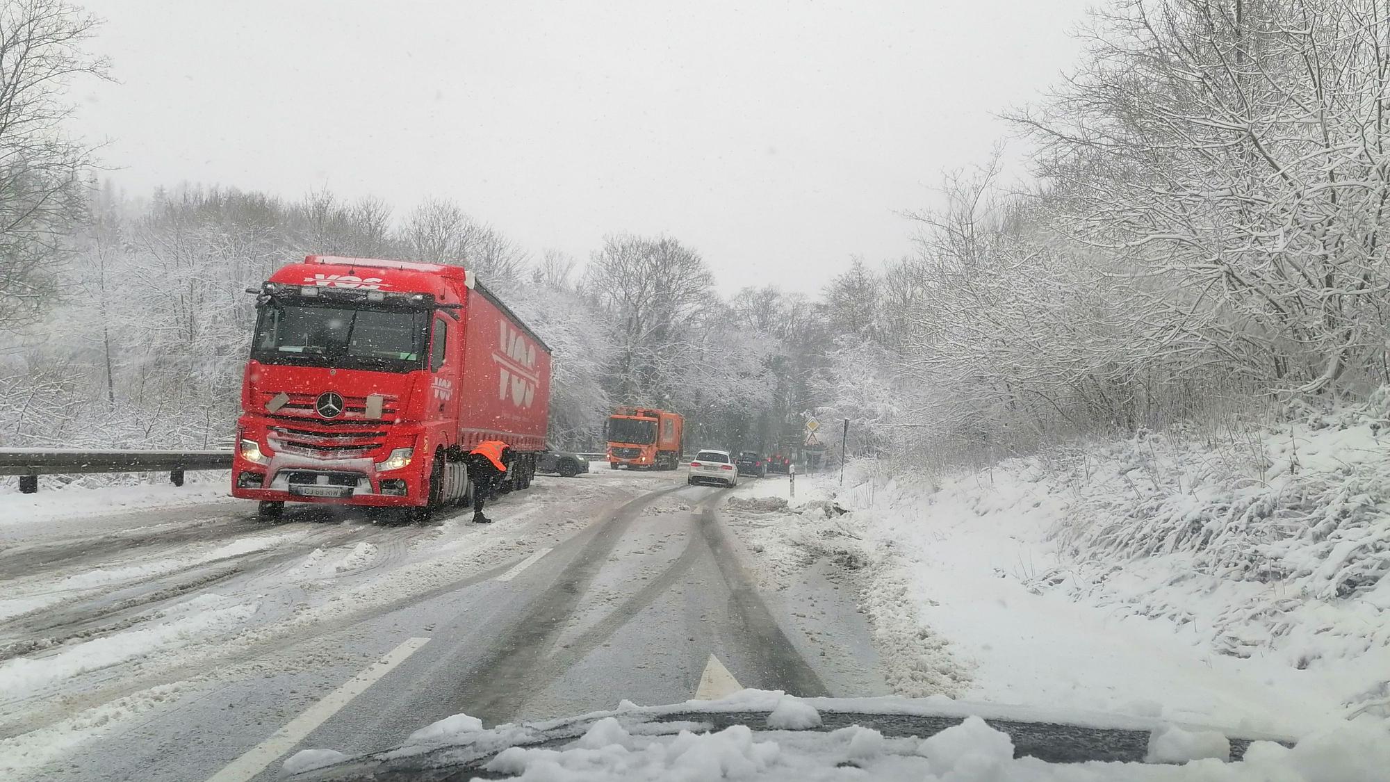 Ein roter Lkw hält auf dem Seitenstreifen einer Schnee-verwehten Straße.