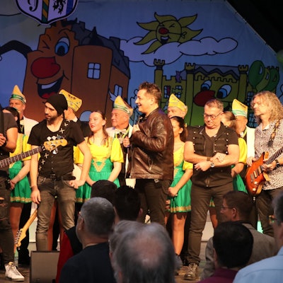 Musiker stehen bei einer Karnevalssitzung auf der Bühne.