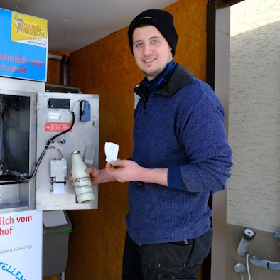 Rainer Berlingen steht mit einer Flasche Milch und einem Kassenbon in der Hand an der „Milchtankstelle“ auf seinem Hof.