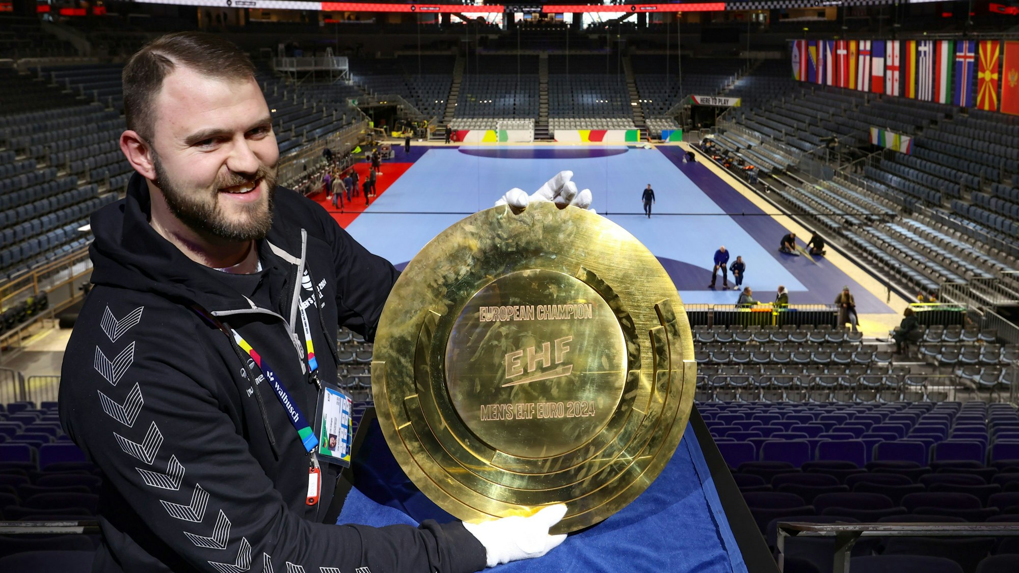 Arena-Sprecher Carsten Heling hält die Trophäe der Handball-Europameisterschaft 2024 hoch.