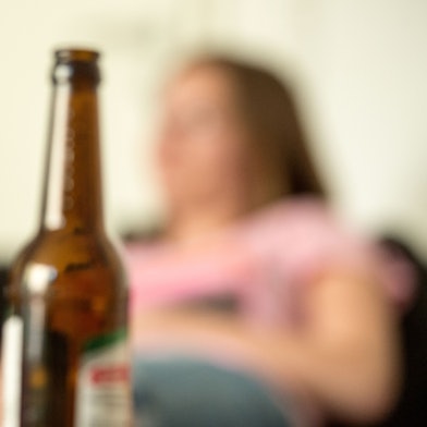 Ein Frau sitzt hinter leeren Bierflaschen.