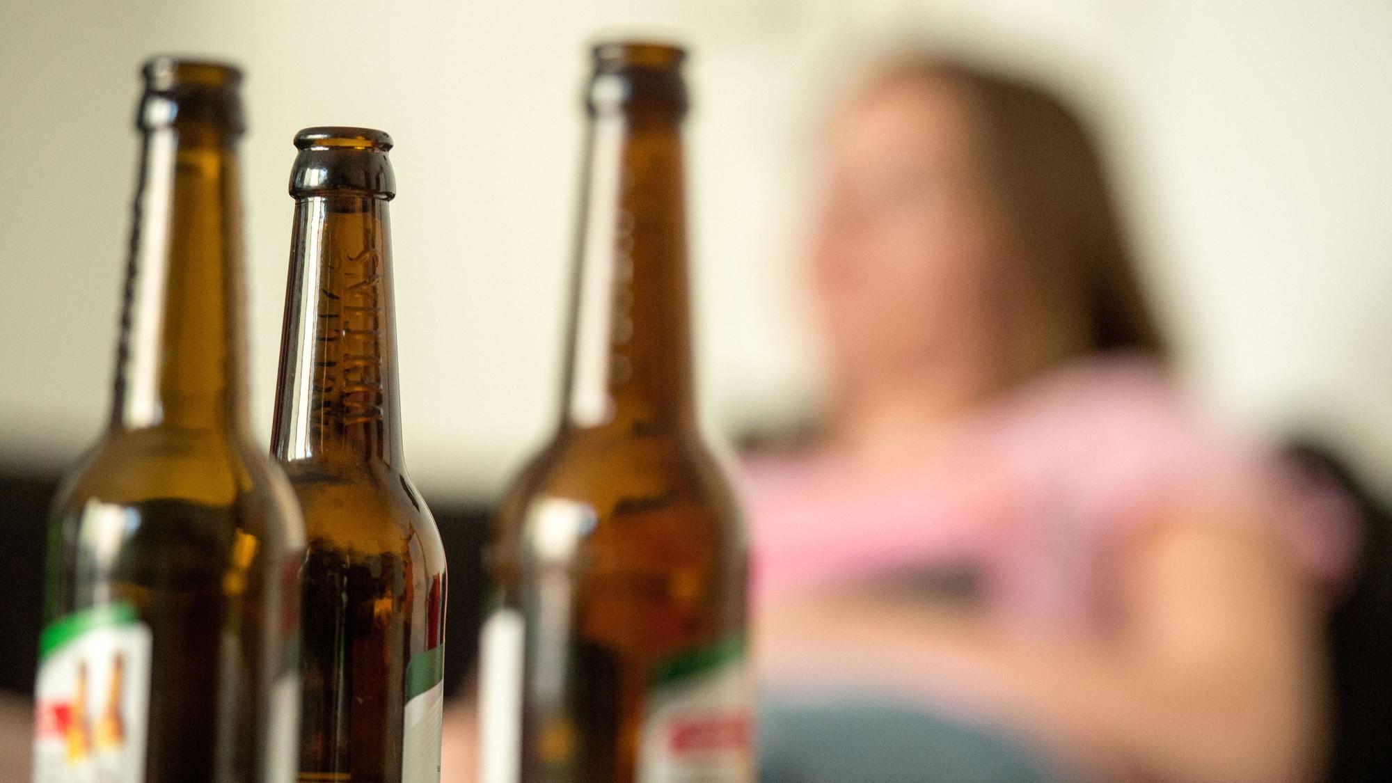 Ein Frau sitzt hinter leeren Bierflaschen.