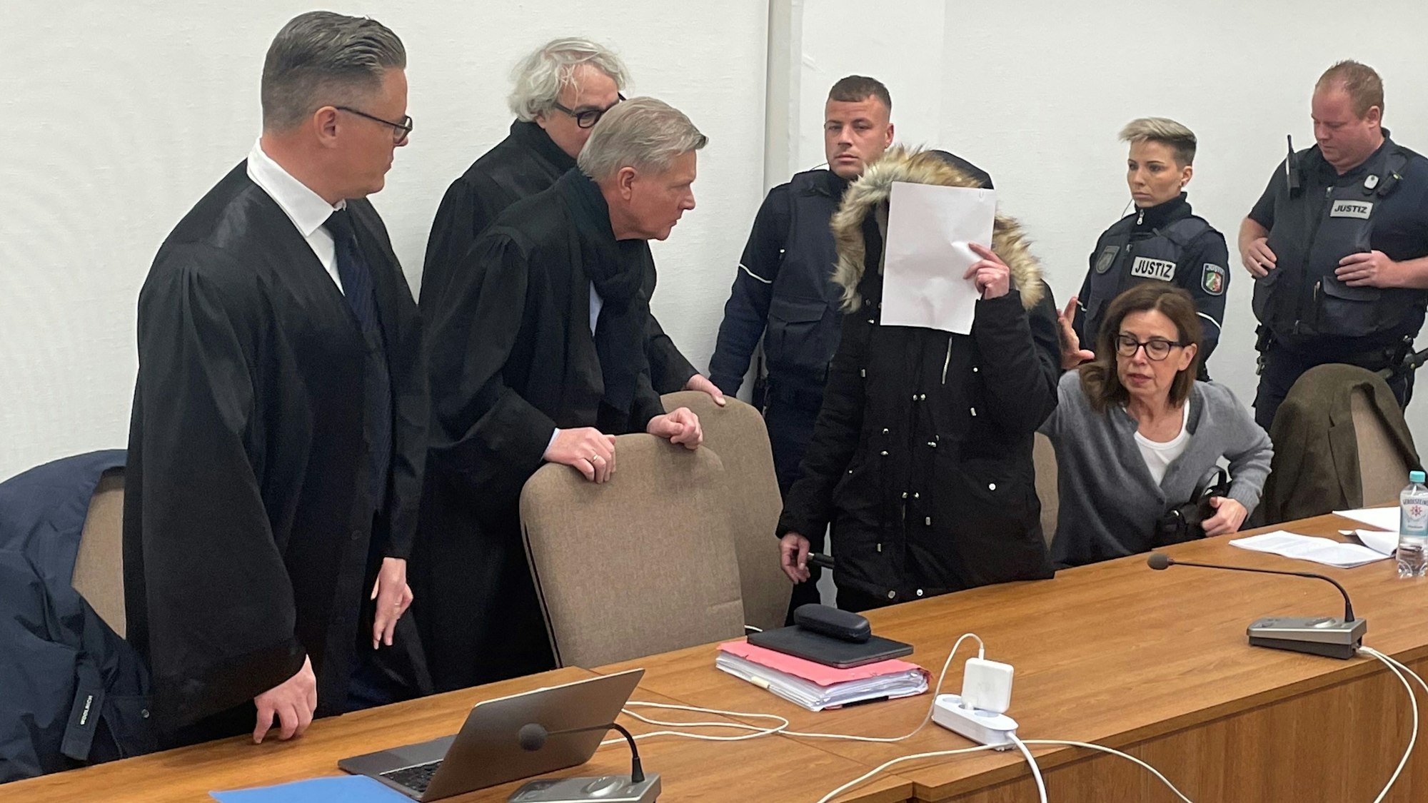 Die Angeklagte wird von Wachtmeistern in den Saal geführt. Sie wird von drei Verteidigern vertreten.
