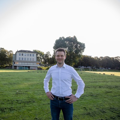 Simon Bujanowski steht vor einem Gebäude mit Umkleiden, das zur Bezirkssportanlage Poll gehört.