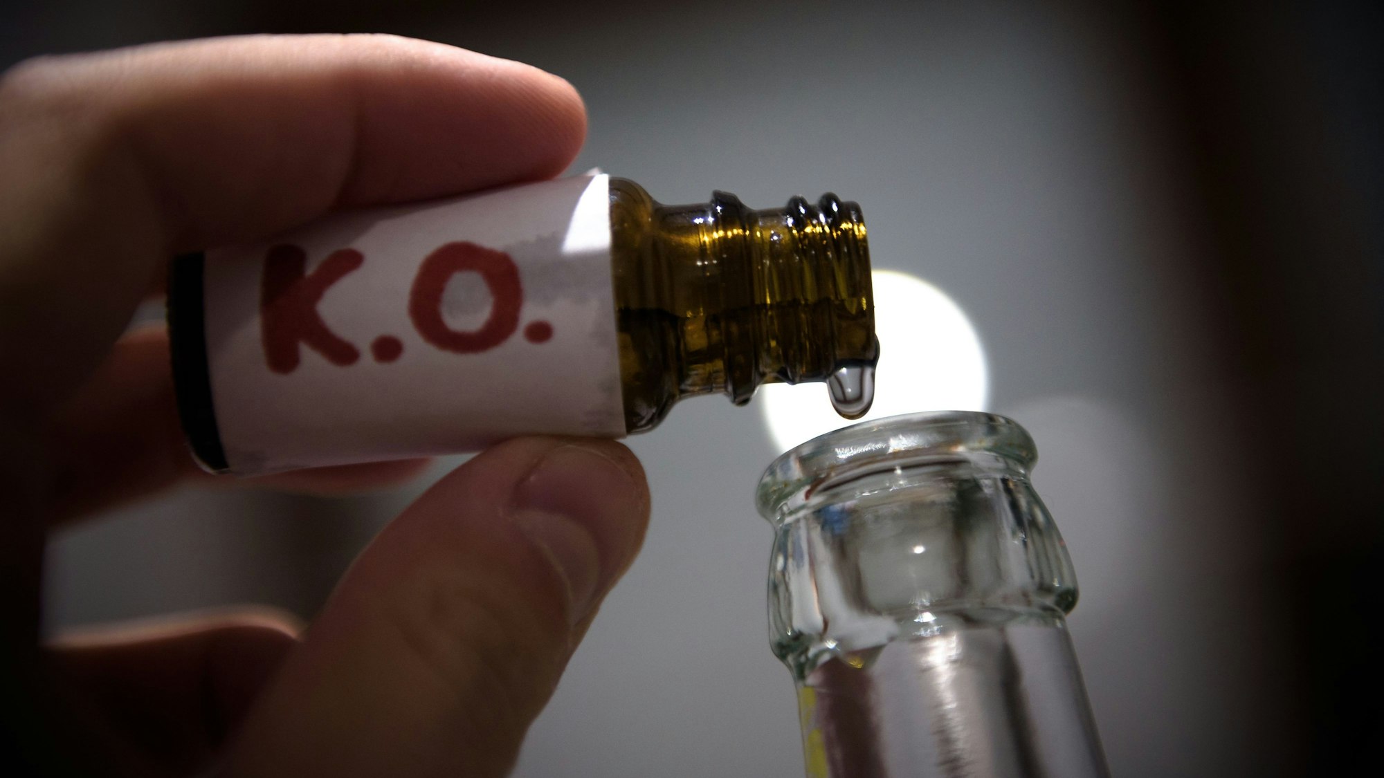 Aus einem Fläschchen mit der Aufschrift „K.O.“ wird eine klare Flüssigkeit in eine Glasflasche geträufelt.