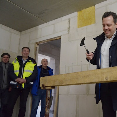 Sacha Reichelt treibt mit einem Hammer einen von sieben Nägeln in einen Balken. Mehrere Zuschauer im Hintergrund lachen.