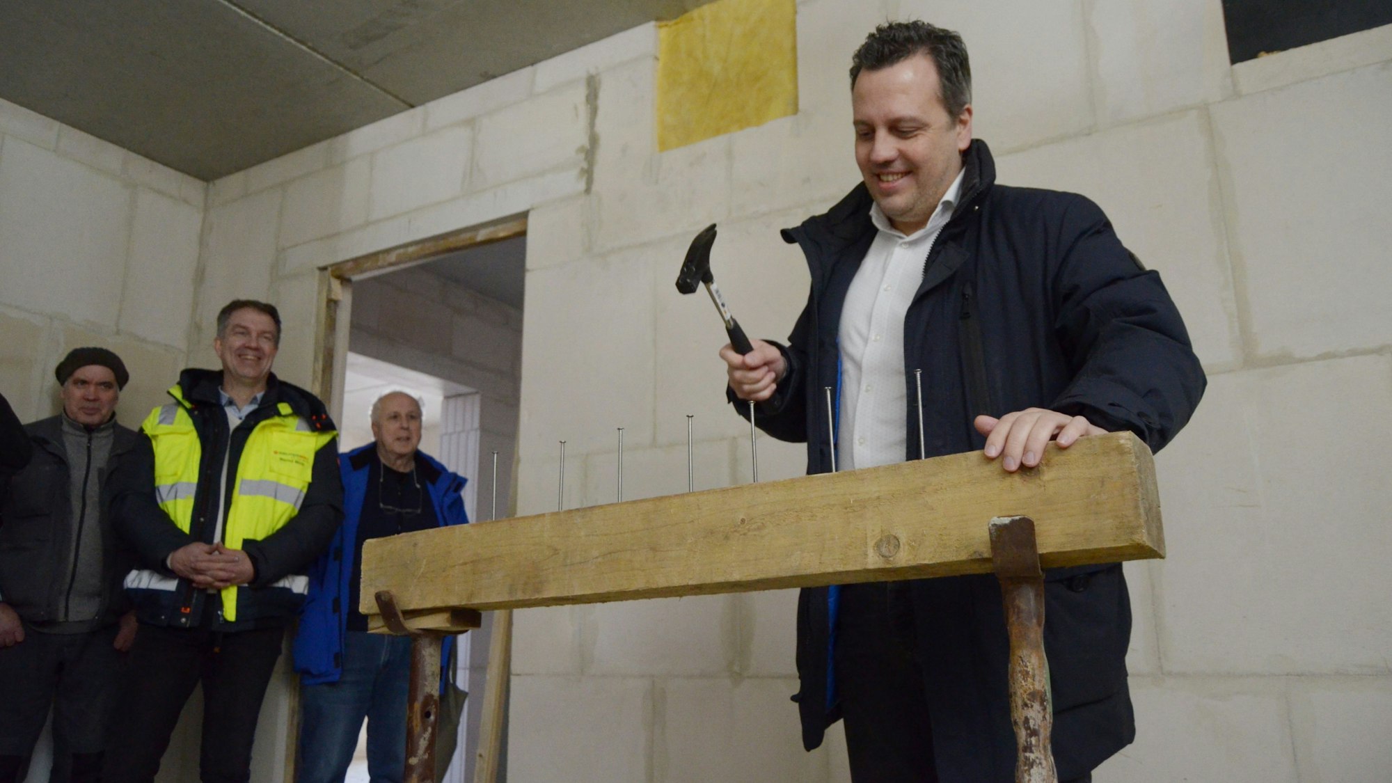 Sacha Reichelt treibt mit einem Hammer einen von sieben Nägeln in einen Balken. Mehrere Zuschauer im Hintergrund lachen.