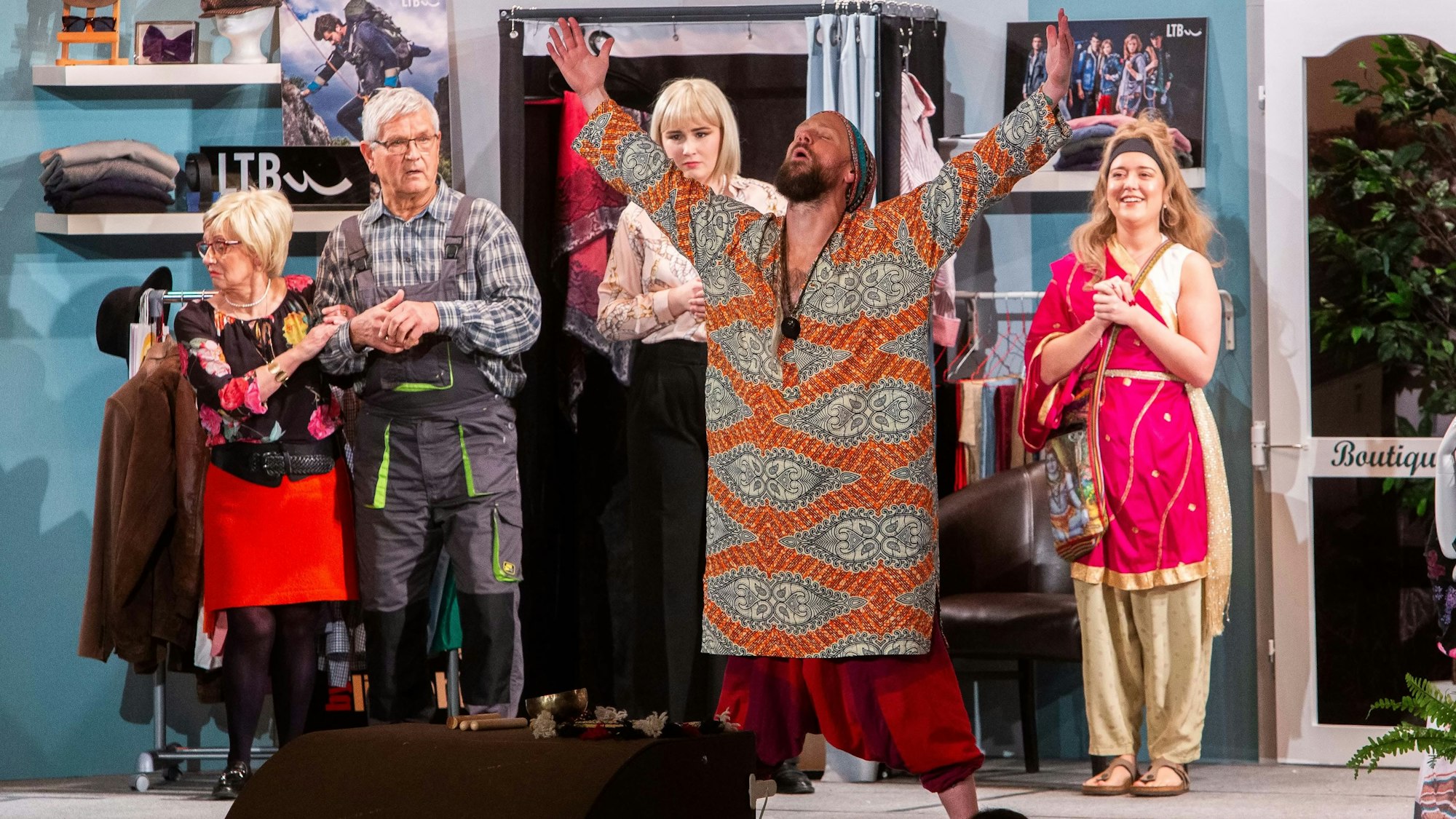 Eine Szene eines Theaterstücks auf einer Bühne. Ein Mann in der Mitte reißt die Hände zum Himmel.