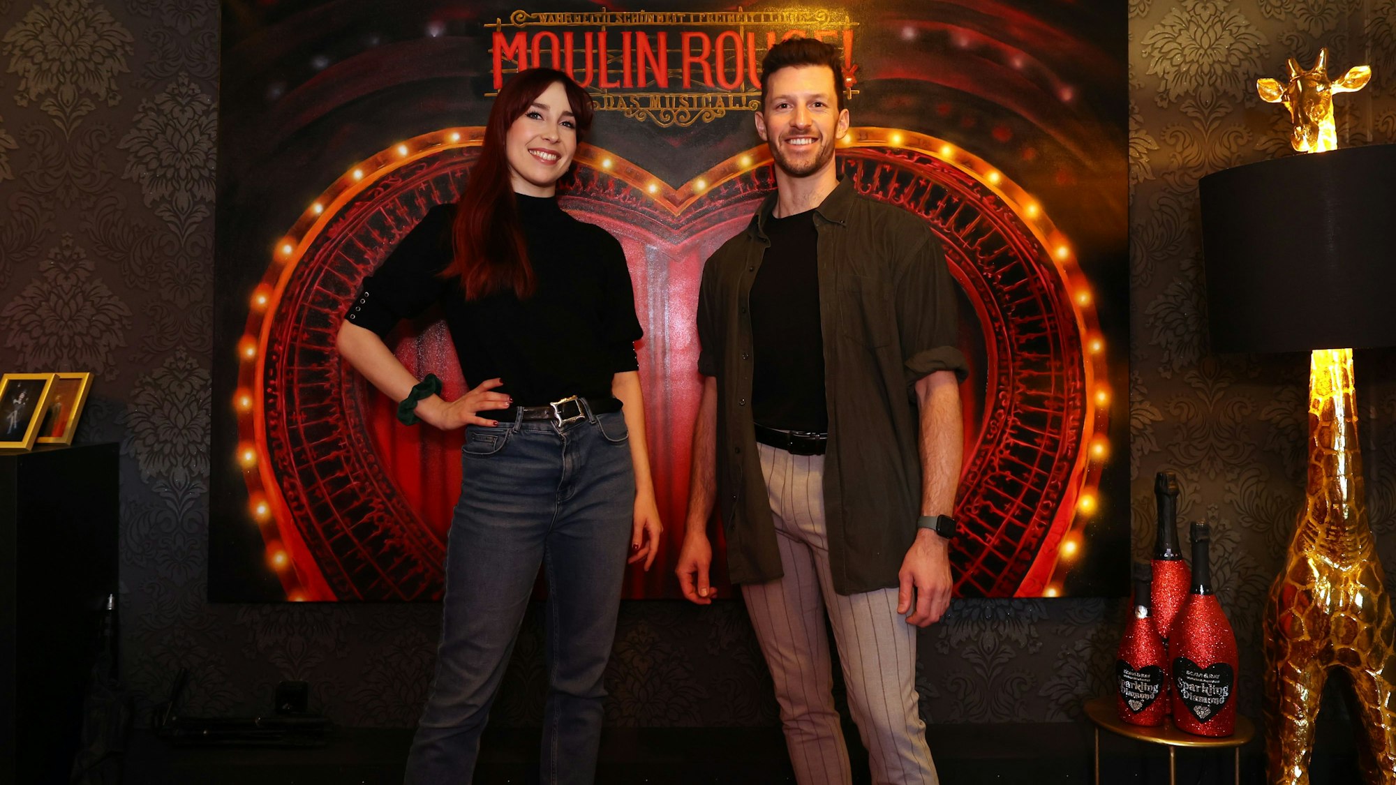 Swing-Darsteller Gabrielle D‘Anthouard und Nathan Saxon im Porträt vor dem Moulin-Rouge-Logo
