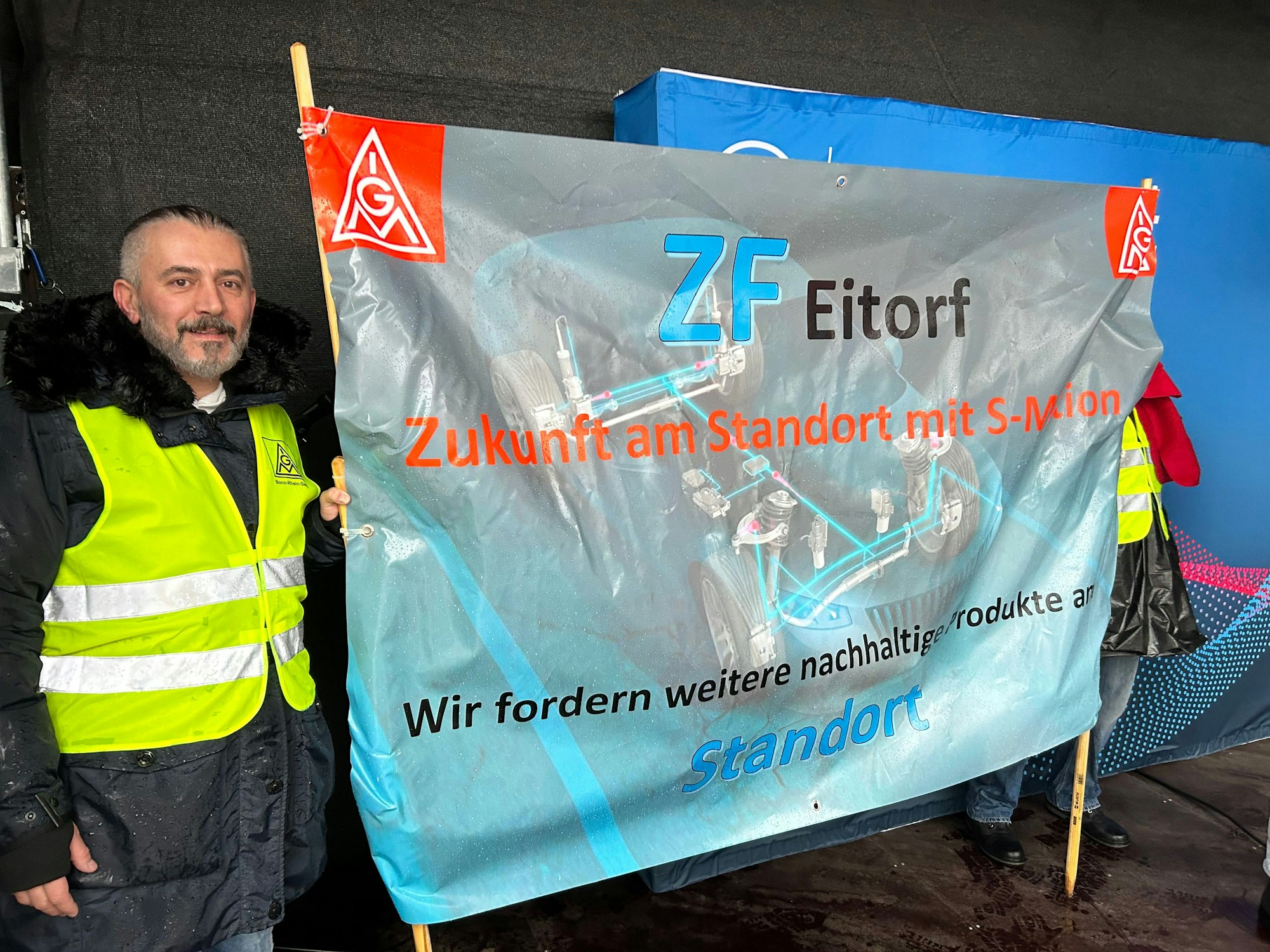 Ein Mann mit gelber Warnweste hält ein Transparent der Gewerkschaft mit der Forderung nach Erhlat des ZF-Standorts Eitorf.