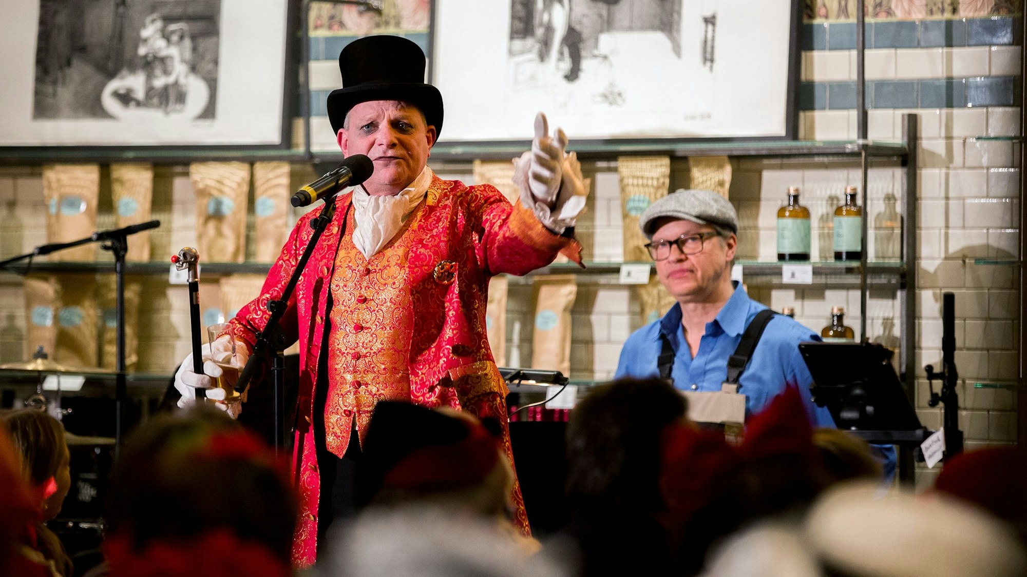 Verkleideter Mann, der vor einem Mikrofon steht, dahinter ein Mann, der am Klavier sitzt