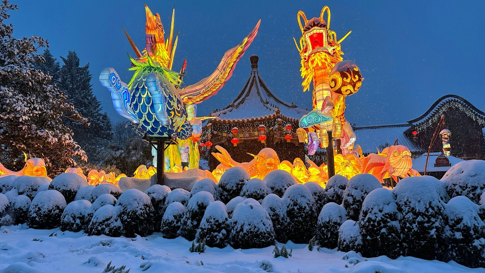 Figuren leuchten vor einer Schneekulisse in der Themenwelt China Town im Phantasialand.