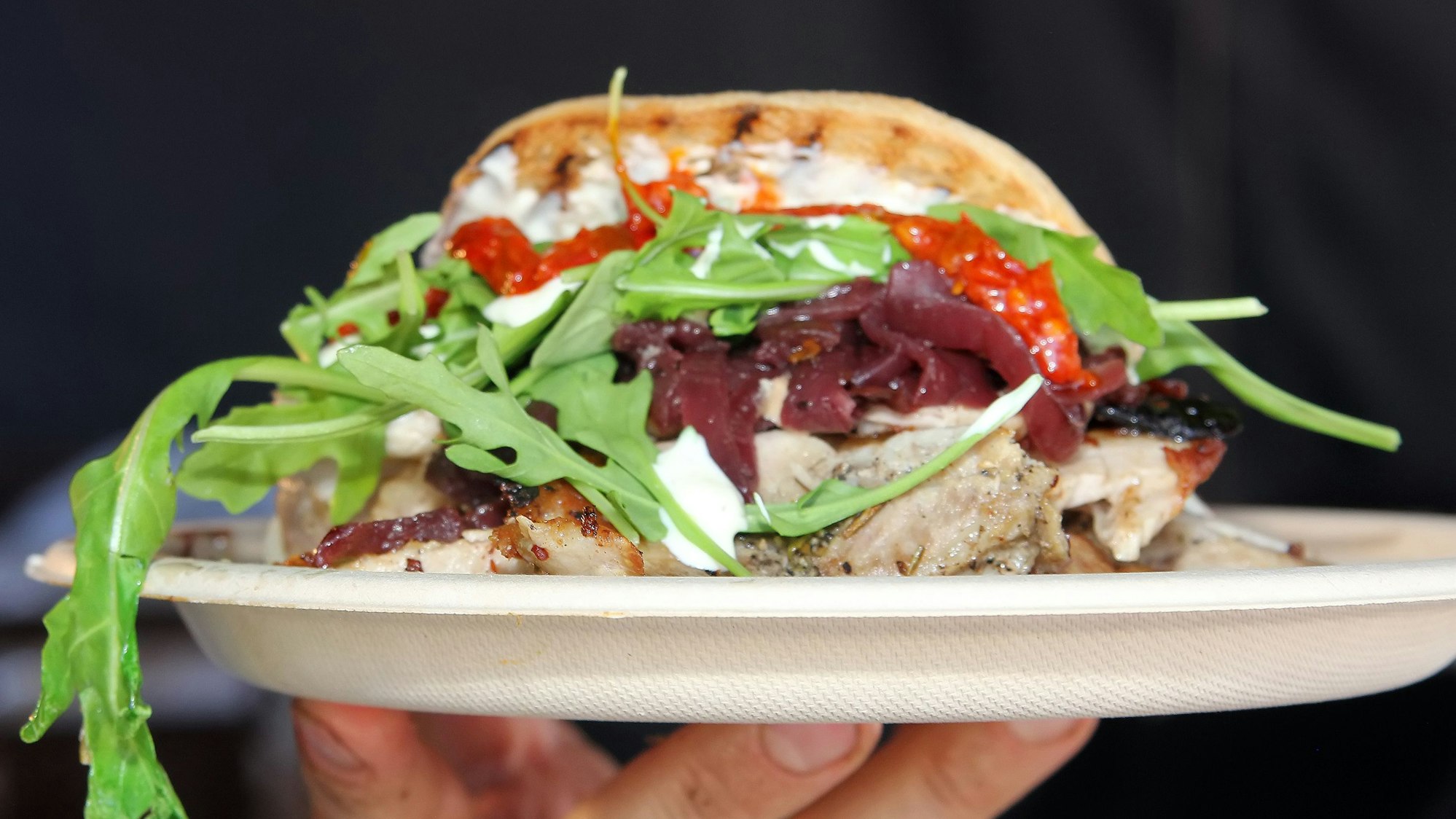 Eine Person hält einen Teller in die Kamera, auf dem eine Burger angerichtet ist.