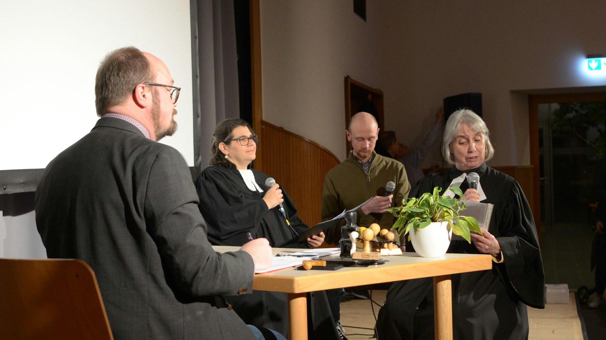 Vier Akteure und Akteurinnen sitzen bei ihrem Sketch auf der Bühne an einem Schreibtisch.