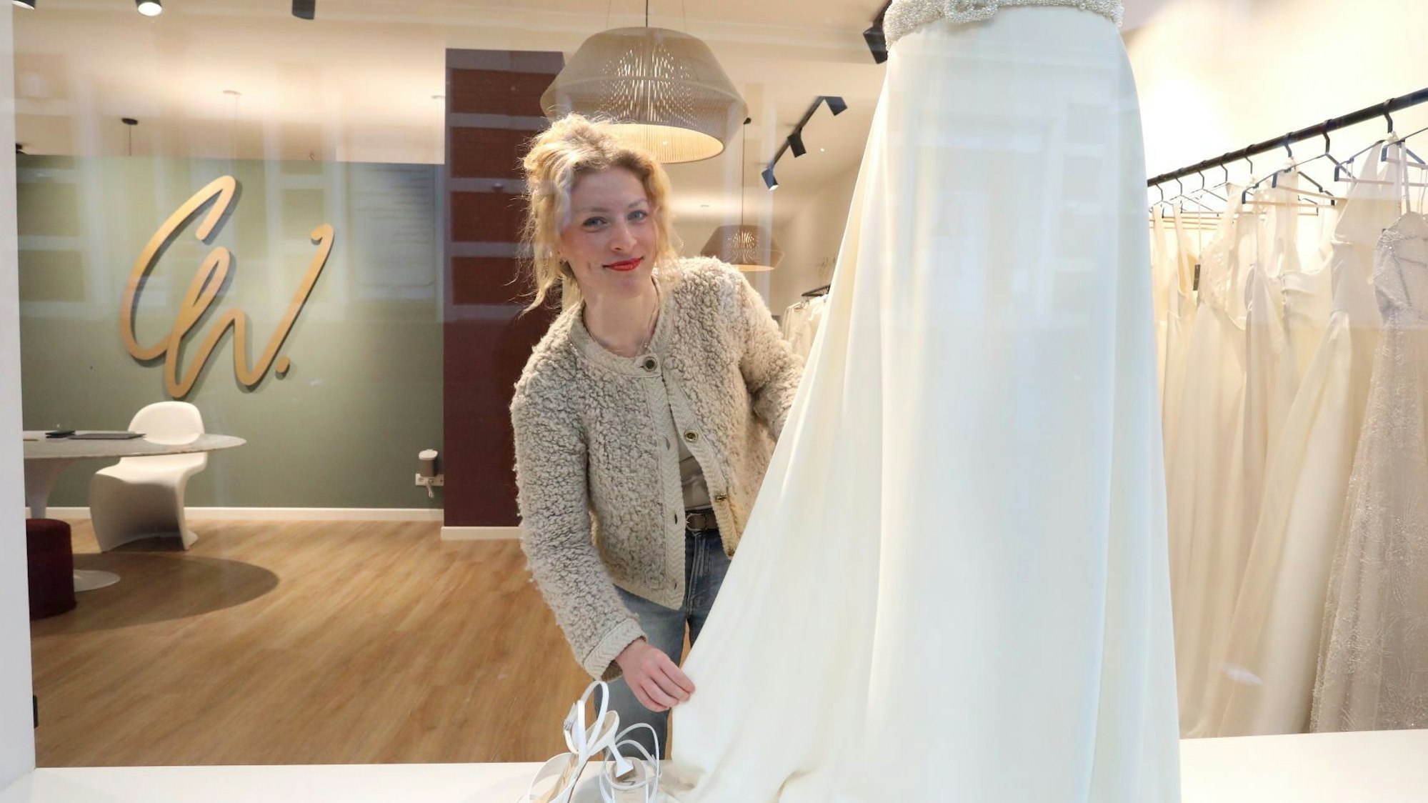 Eine Frau drapiert im Schaufenster ihres Brautmodengeschäfts ein weißes Hochzeitskleid.