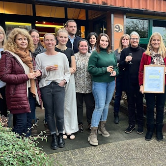 Männer und Frauen stehen vor einem Gebäude, eine Frau hält ein Zertifikat.