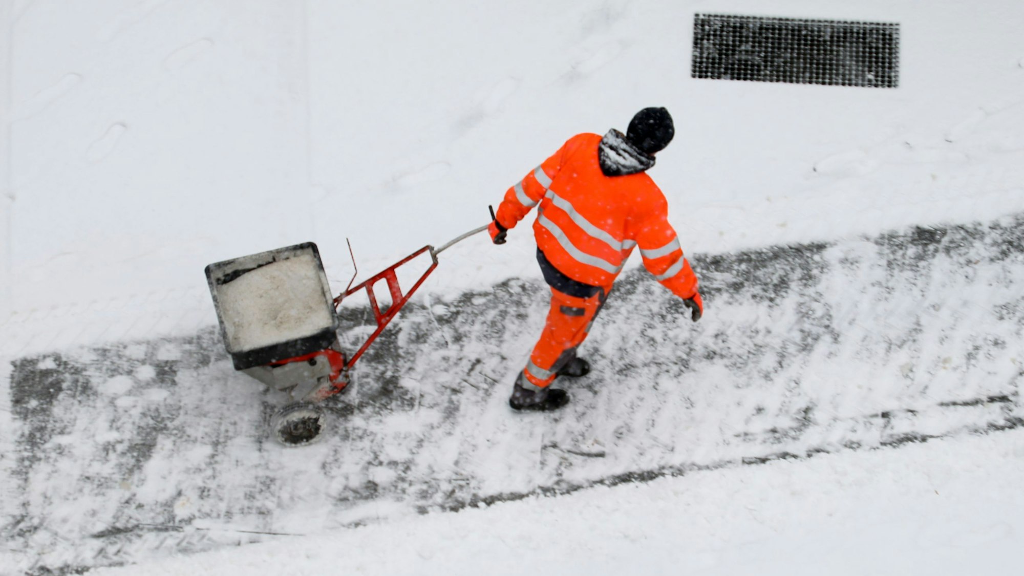 Ein Winterdienstmitarbeiter der Stadt Bergisch Gladbach zieht einen Handstreuwagen mit Salz hinter sich her.