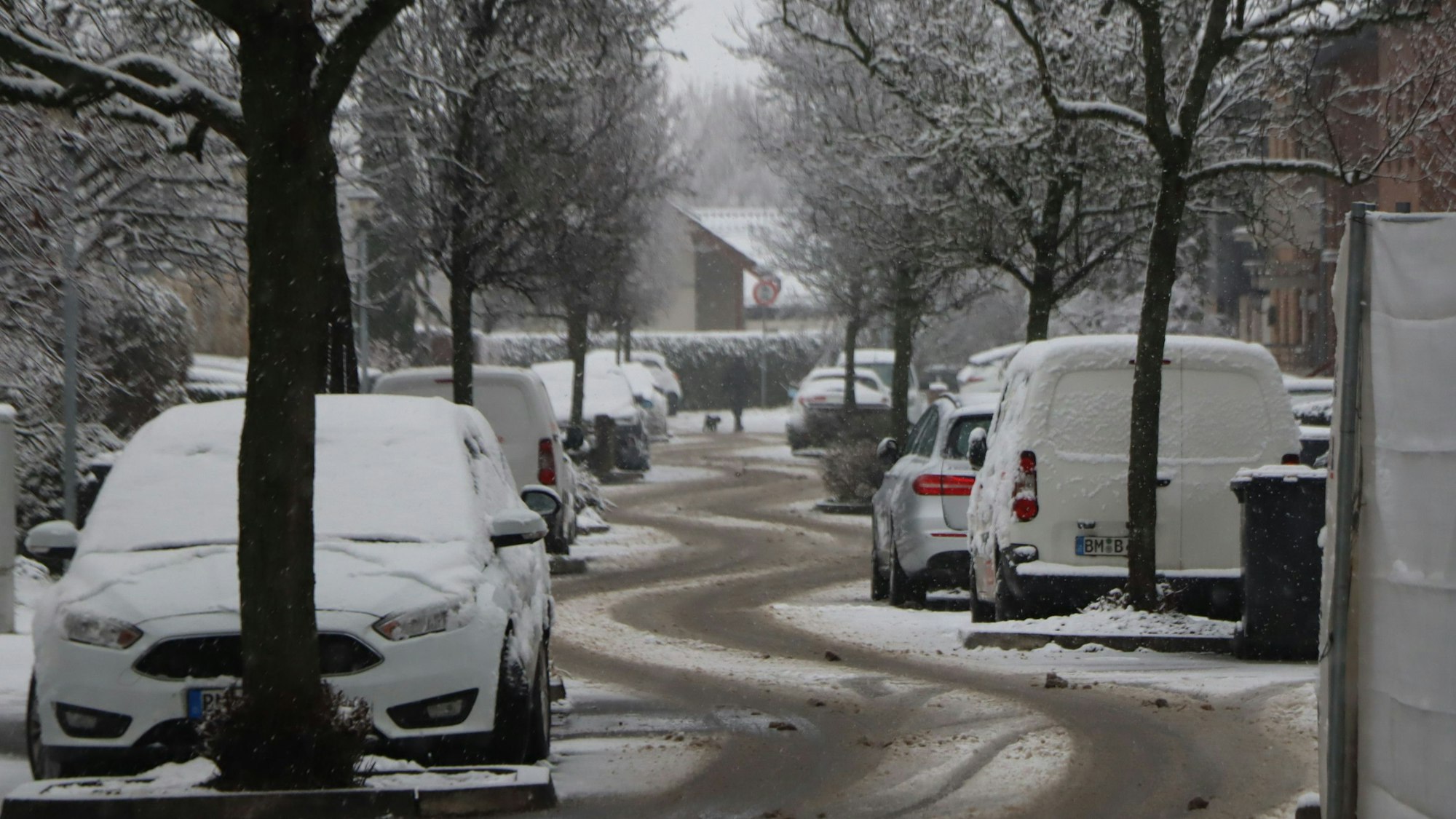 Eine verschneite Straße mit deutlichen Reifenspuren.