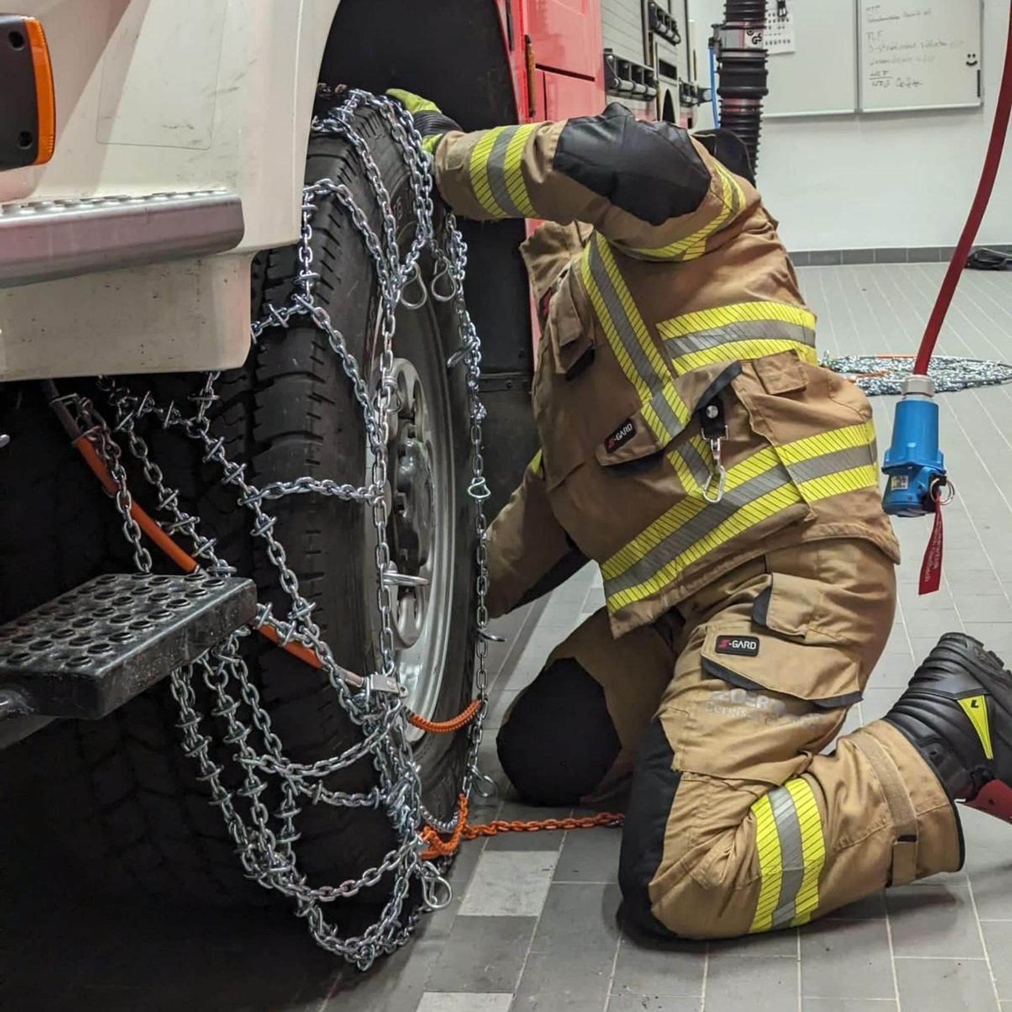 Ein Feuerwehrmann zieht eine Schneekette auf das Rad eines Feuerwehrfahrzeugs auf.