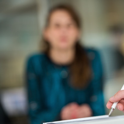 Ein Mann hält in einem Büro einen Kugelschreiber, während im Hintergrund eine Frau sitzt.