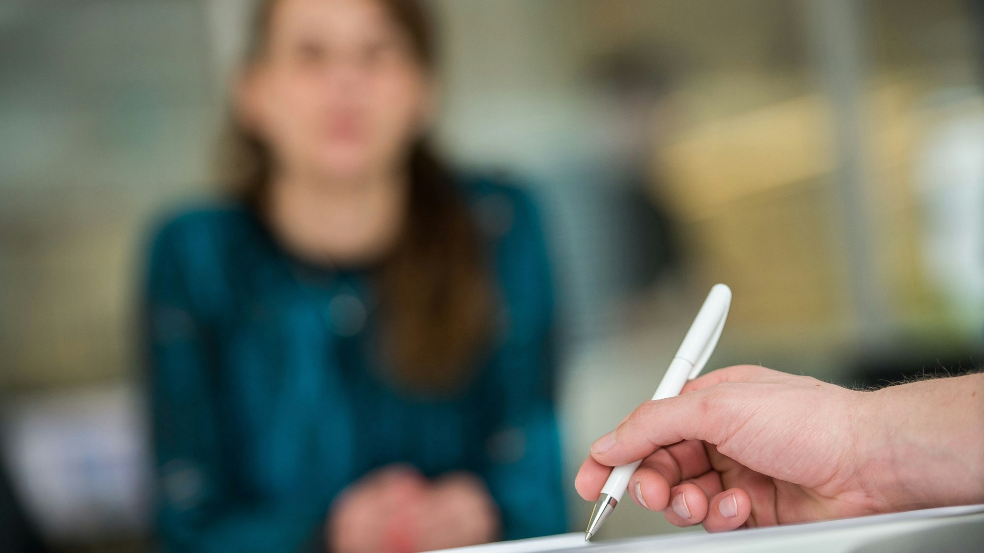 Ein Mann hält in einem Büro einen Kugelschreiber, während im Hintergrund eine Frau sitzt.