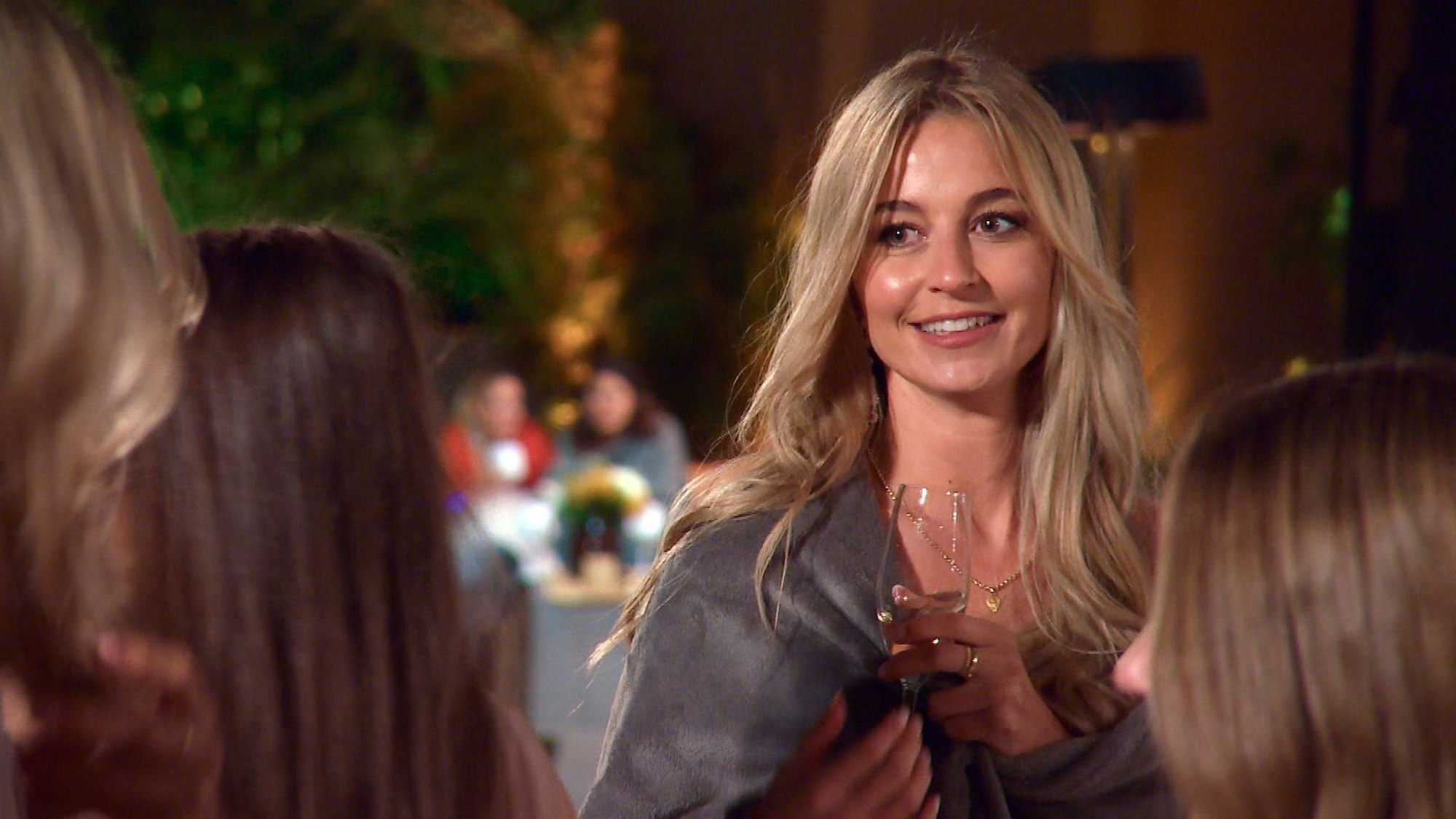 Eine Frau lächelt und blickt an der Kamera vorbei. Sie hat ein Glas Sekt in der Hand.