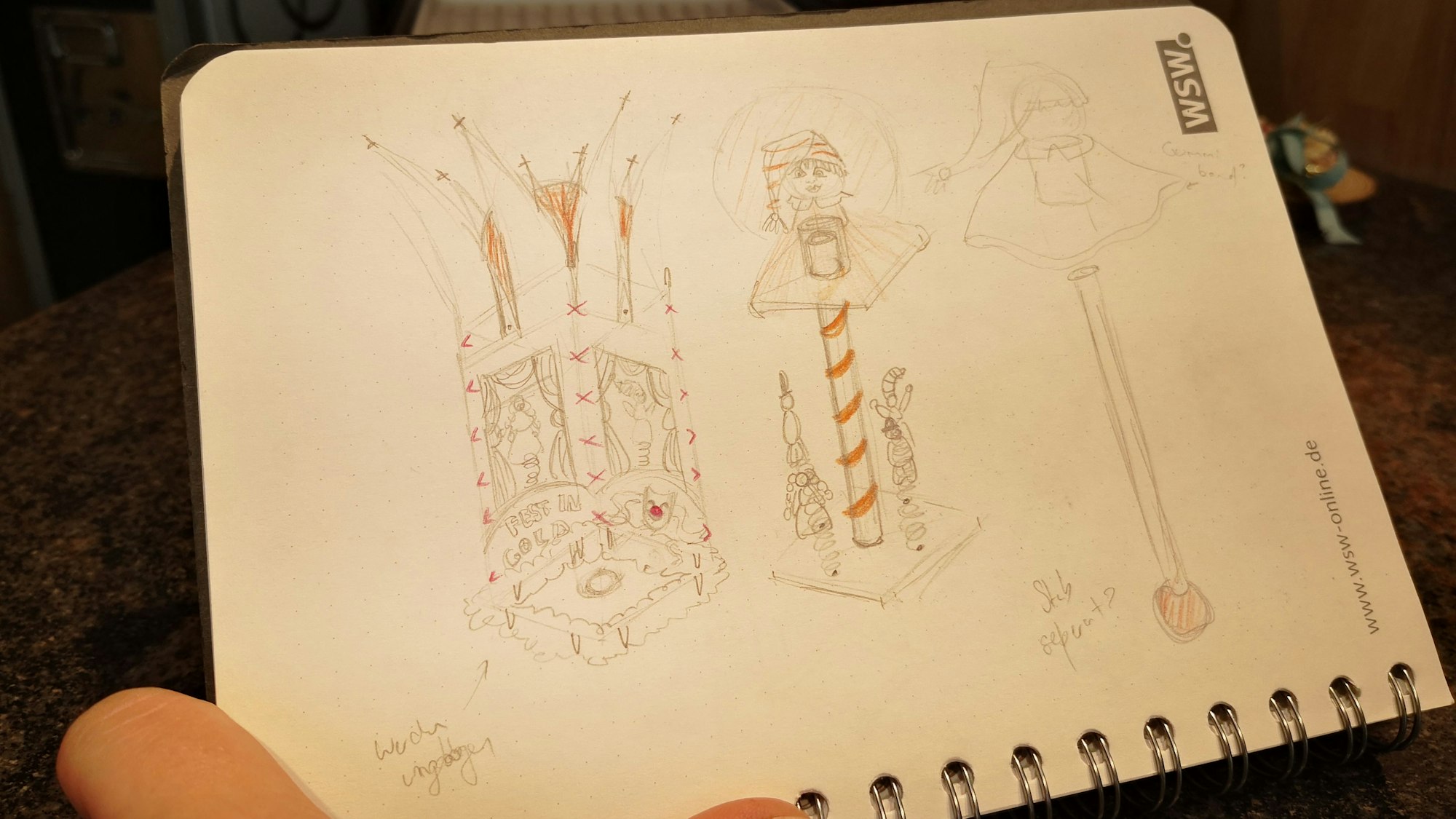 Auf einem Notizbuch sind Bleistiftskizzen des Ordens-Entwurfs zu sehen.