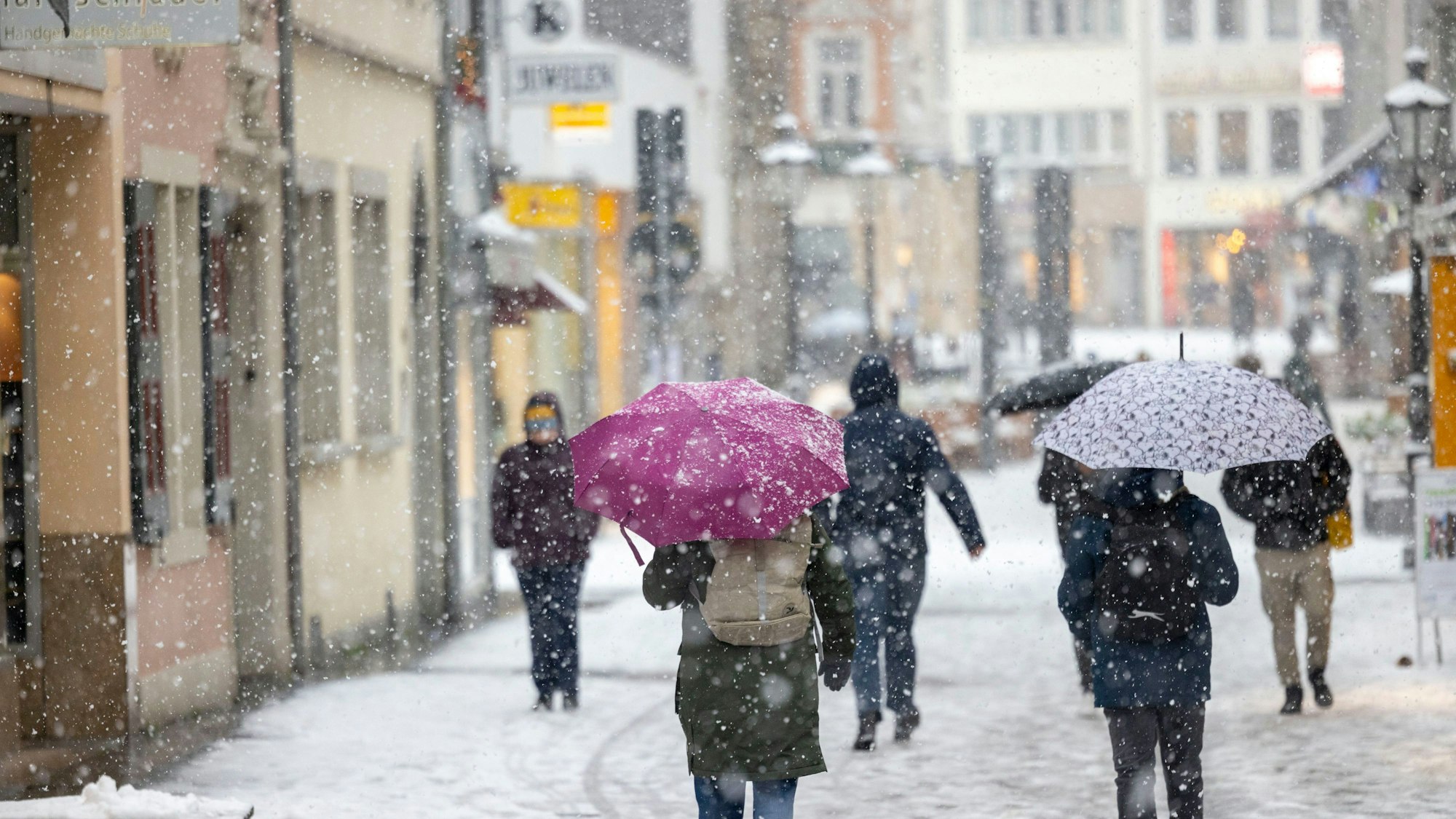 Menschen gehen bei dichtem Schneefall durch die Bonner Innenstadt.