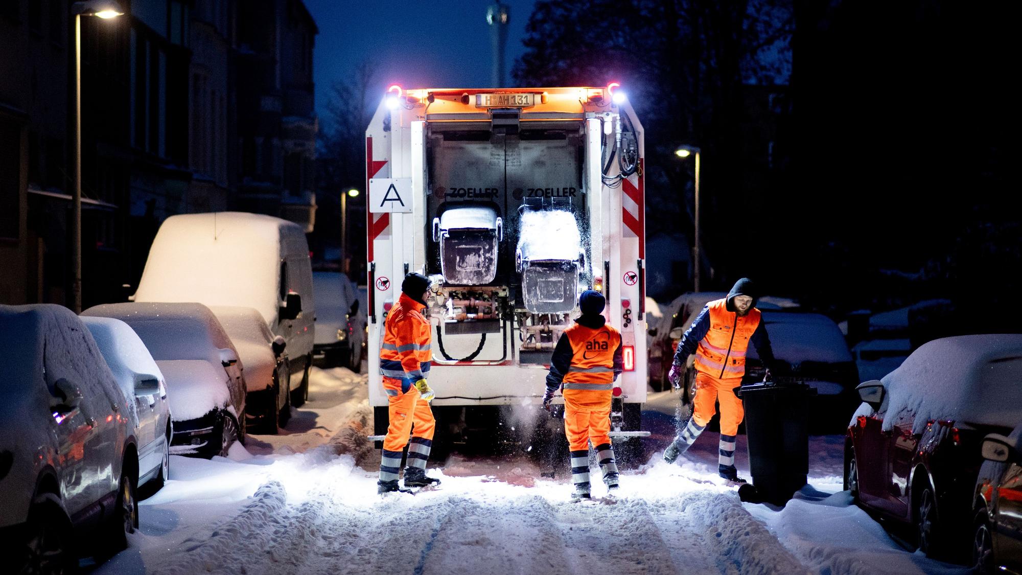 Ein Müllwagen fährt über eine zugeschneite Straße.