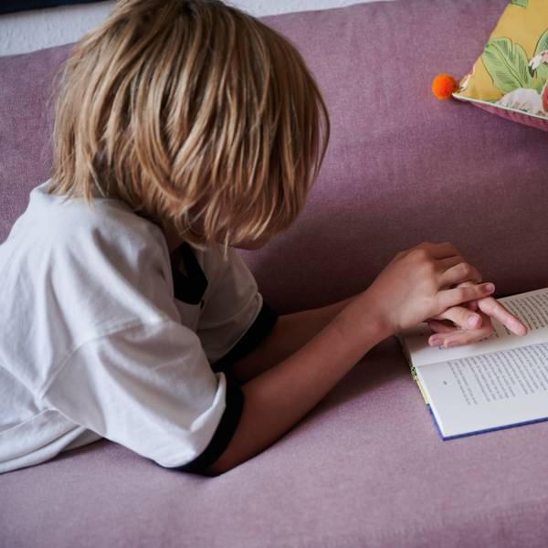 Ein Junge liegt mit einem Buch auf einem Sofa.