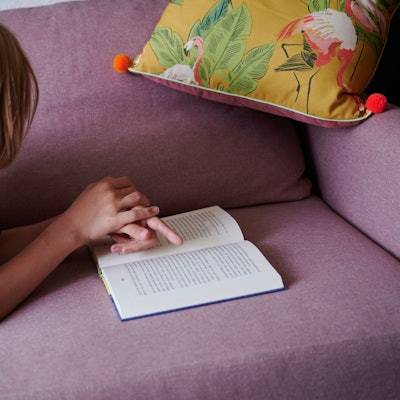 Ein Junge liegt mit einem Buch auf einem Sofa.
