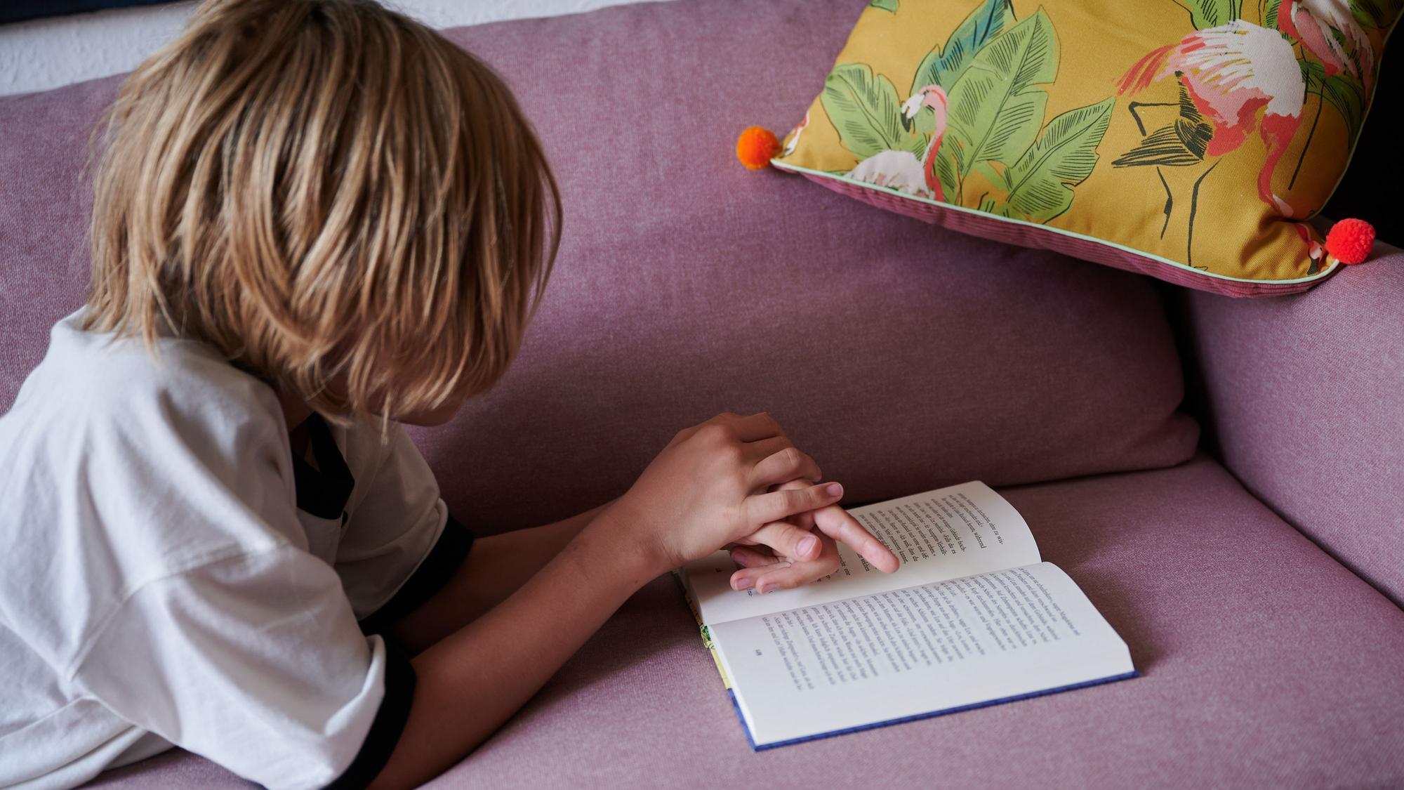 Ein Junge liegt mit einem Buch auf einem Sofa.