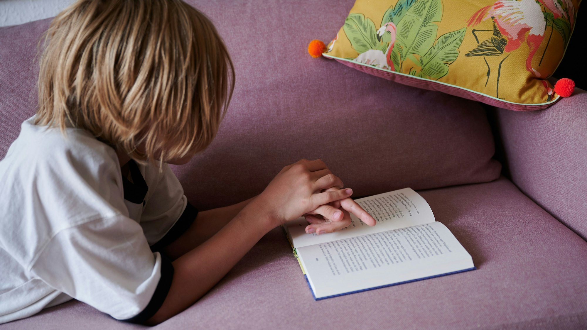 Ein Kind liegt auf dem Sofa und liest ein Buch.