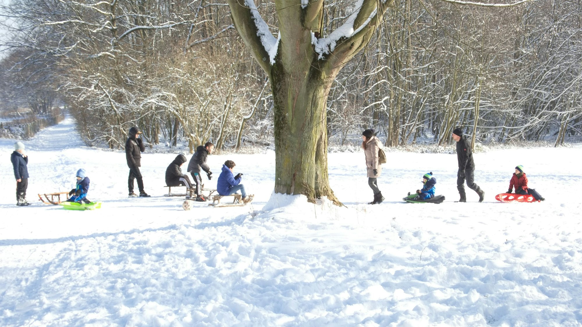 Zu sehen sind Männer, Frauen und Kinder auf Schlitten im Schnee.