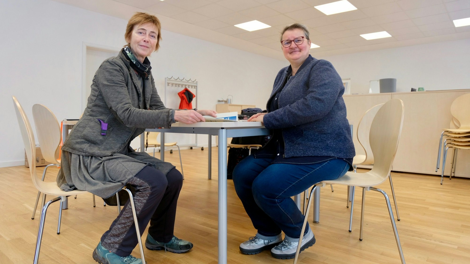 Zwei Frauen sitzen an einem Tisch in einem großen Raum.