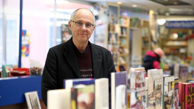 Ein Mann mit Brille steht hinter einem Tisch, auf dem viele Bücher ausgestellt sind.
