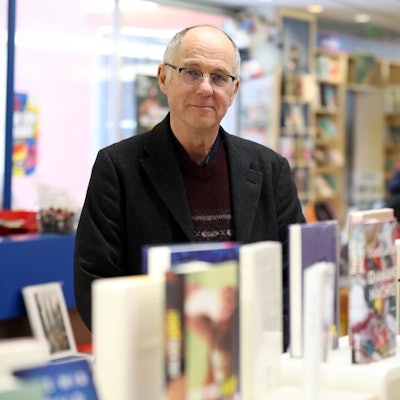 Ein Mann mit Brille steht hinter einem Tisch, auf dem viele Bücher ausgestellt sind.