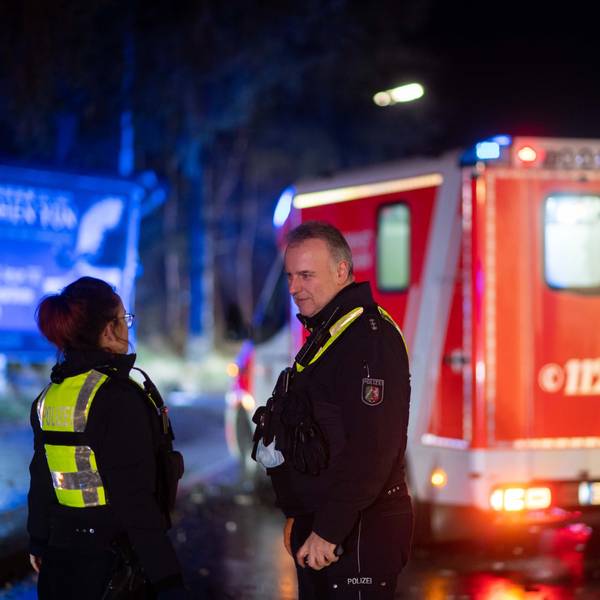 Zwei Polizisten stehen bei einem Einsatz in der Dunkelheit vor einem Rettungswagen.