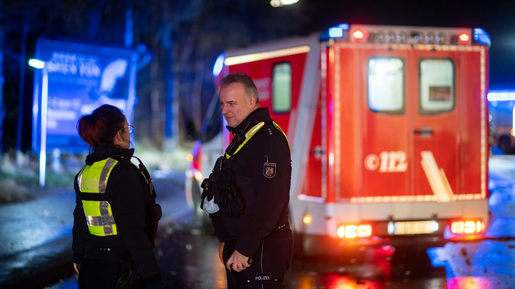 Zwei Polizisten stehen bei einem Einsatz in der Dunkelheit vor einem Rettungswagen.