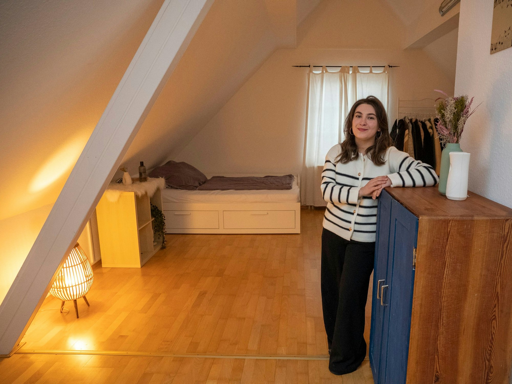 Eine junge Frau steht in einem Zimmer mit Dachschräge und blickt in die Kamera.