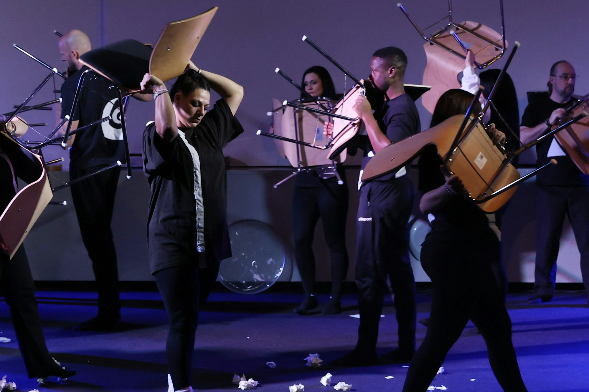 Die Schauspielerinnen und Schauspieler der JVA Ossendorf laufen kreuz und quer über die Bühne und tragen Stühle mit sich.