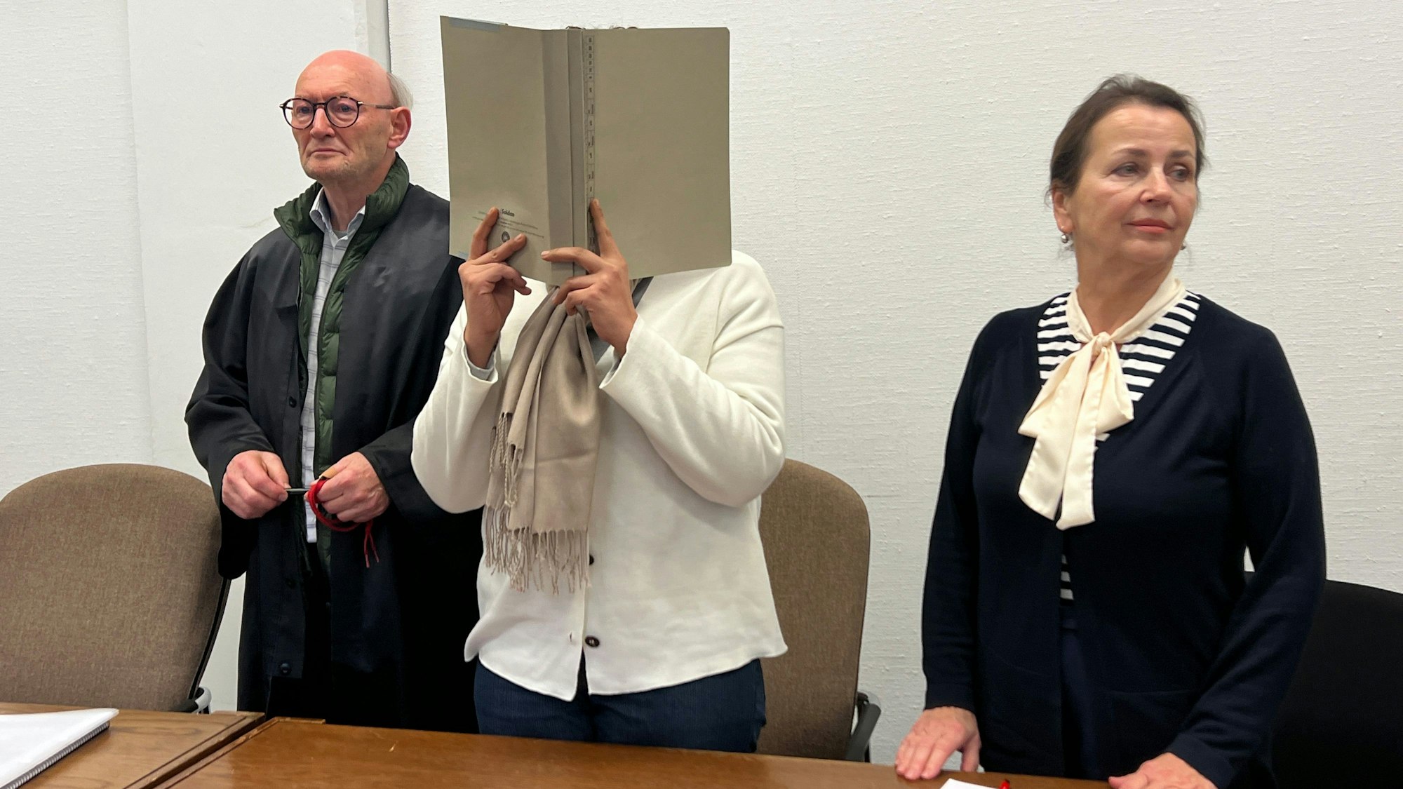 Schockanrufe bei meist alten Frauen waren ihr Metier, im Gerichtssaal verbirgt die 25-jährige Angeklagte ihr Gesicht, als sie mit Rechtsanwalt und Dolmetscherin an der Anklagebank steht.