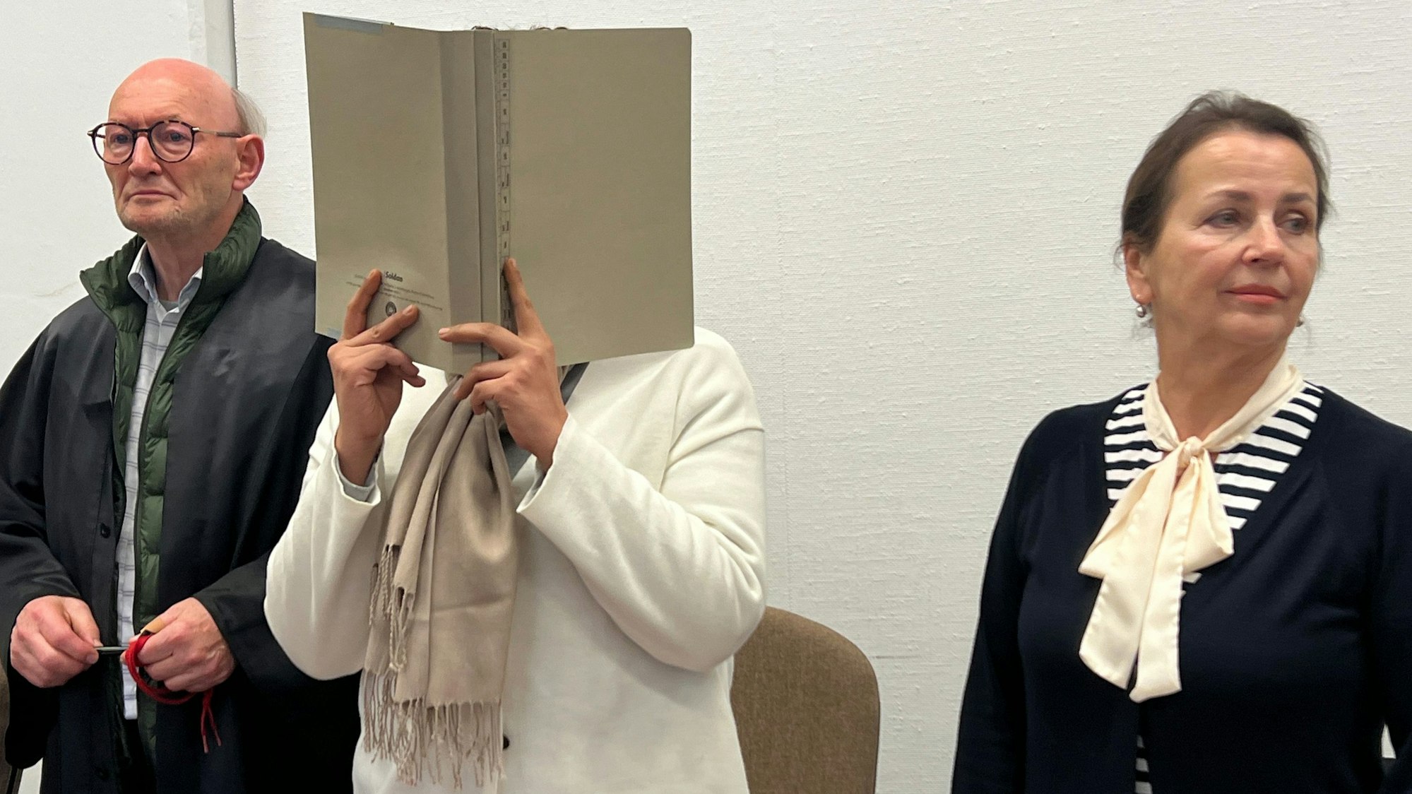 Gegen eine an Schockanrufen beteiligte Frau ist am 25. April 2024 das Urteil gesprochen worden. Sie steht, getarnt hinter einem Aktendeckel, zwischen ihrem Verteidiger Günter Teworte und der Dolmetscherin im Gerichtssaal.