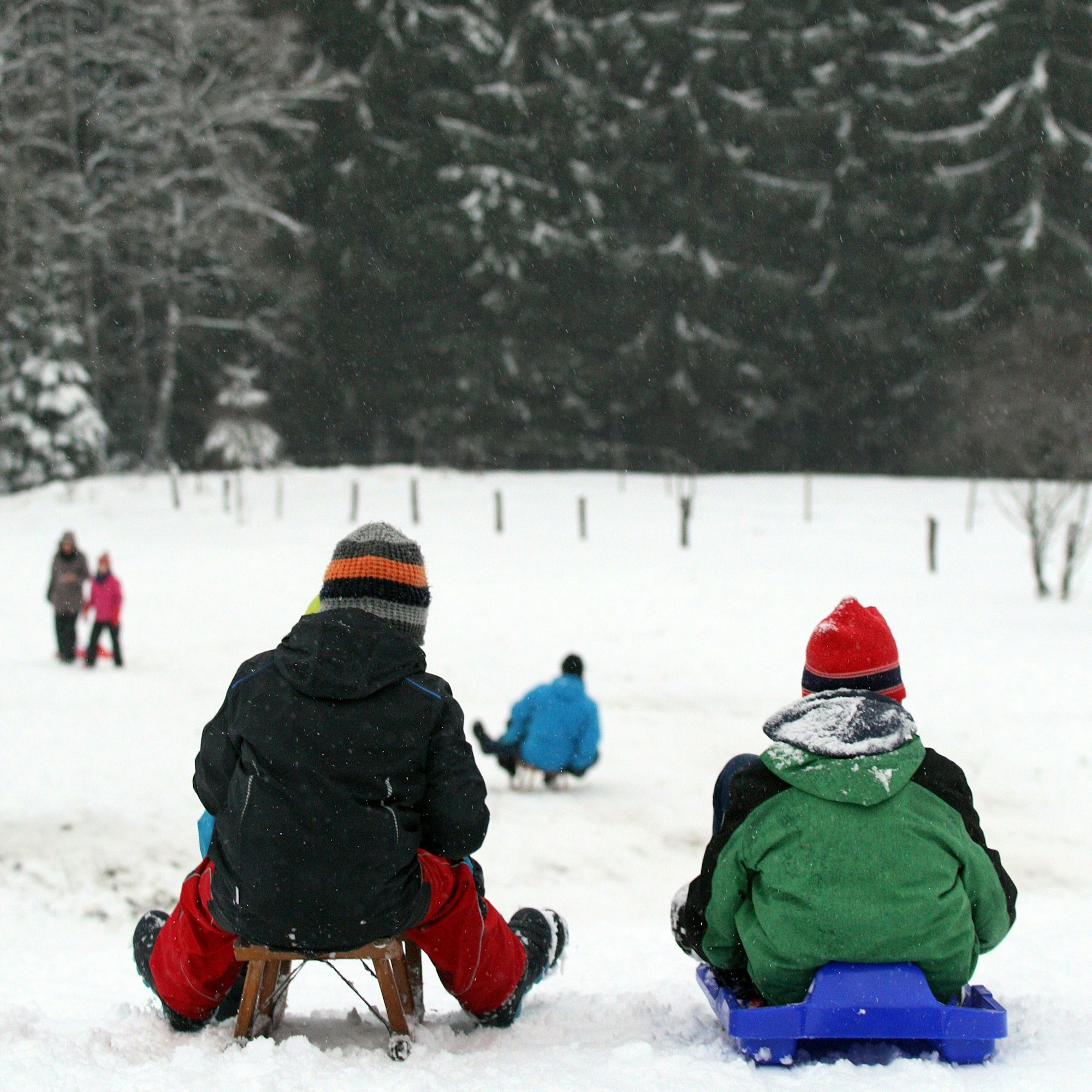Zwei Kinder stehen an einem Schlittenhang und wollen gerade losfahren.