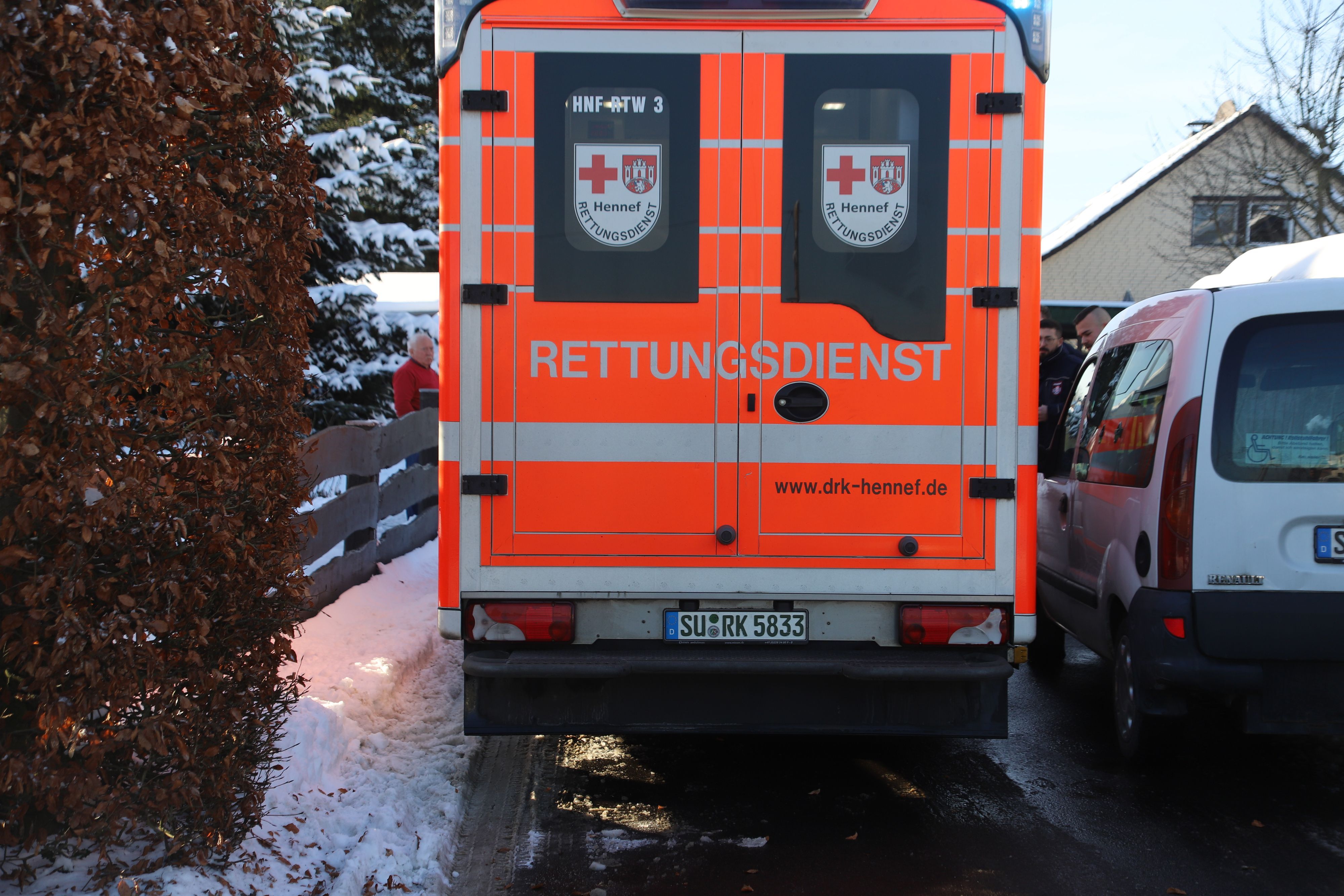 Ein Rettungsfahrzeug fährt durch eine schneebedeckte Straße nur Zentimeter an einem geparkten Fahrzeug vorbei.