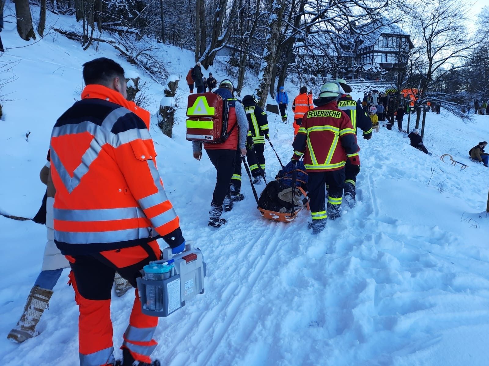 Rettungskäfte ziehen eine Schleifkorbtrage durch den tiefen Schnee einen Weg hinauf.