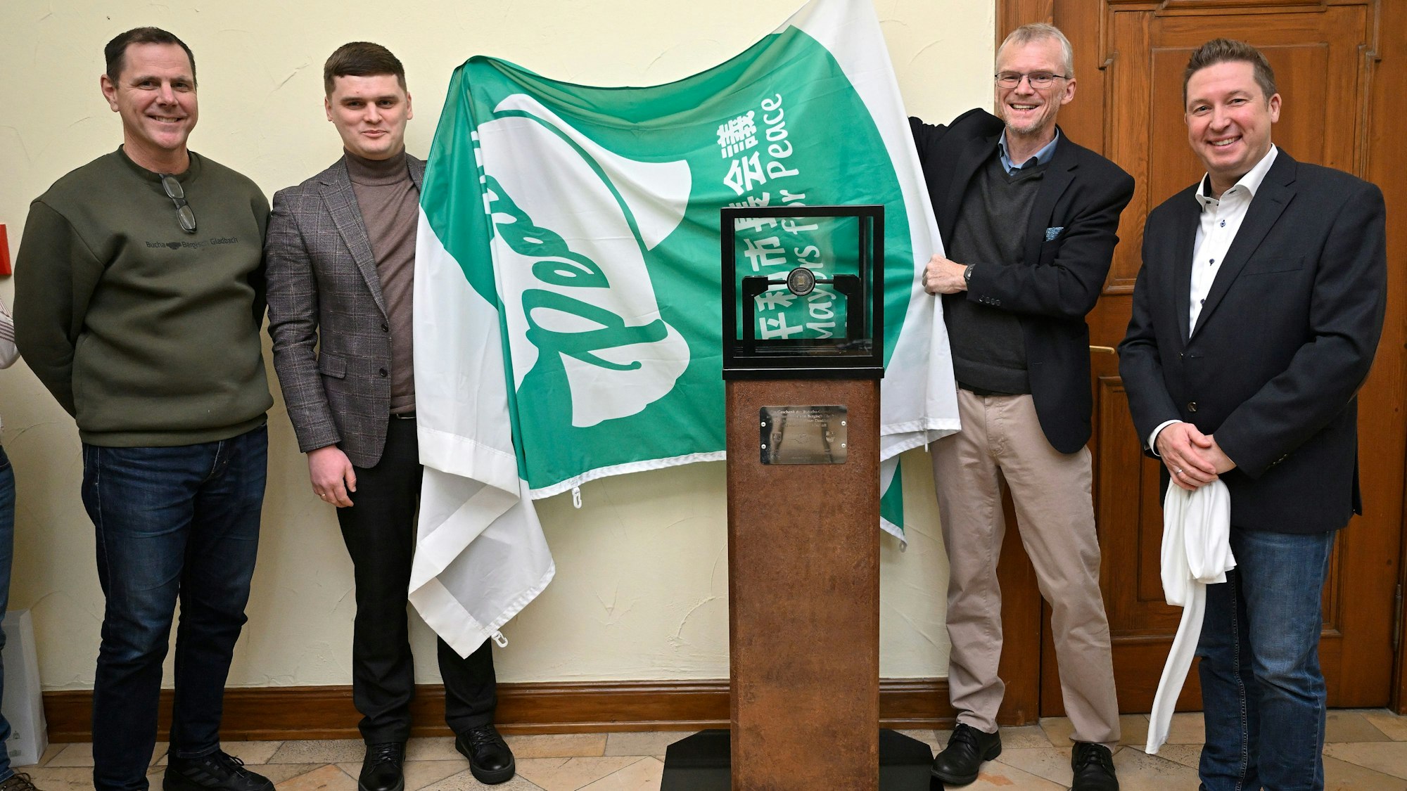 Vier Menschen enthüllen eine Stele, die ein Gastgeschenk der ukrainischen Stadt Butscha an die Partnerstadt Bergisch Gladbach ist.