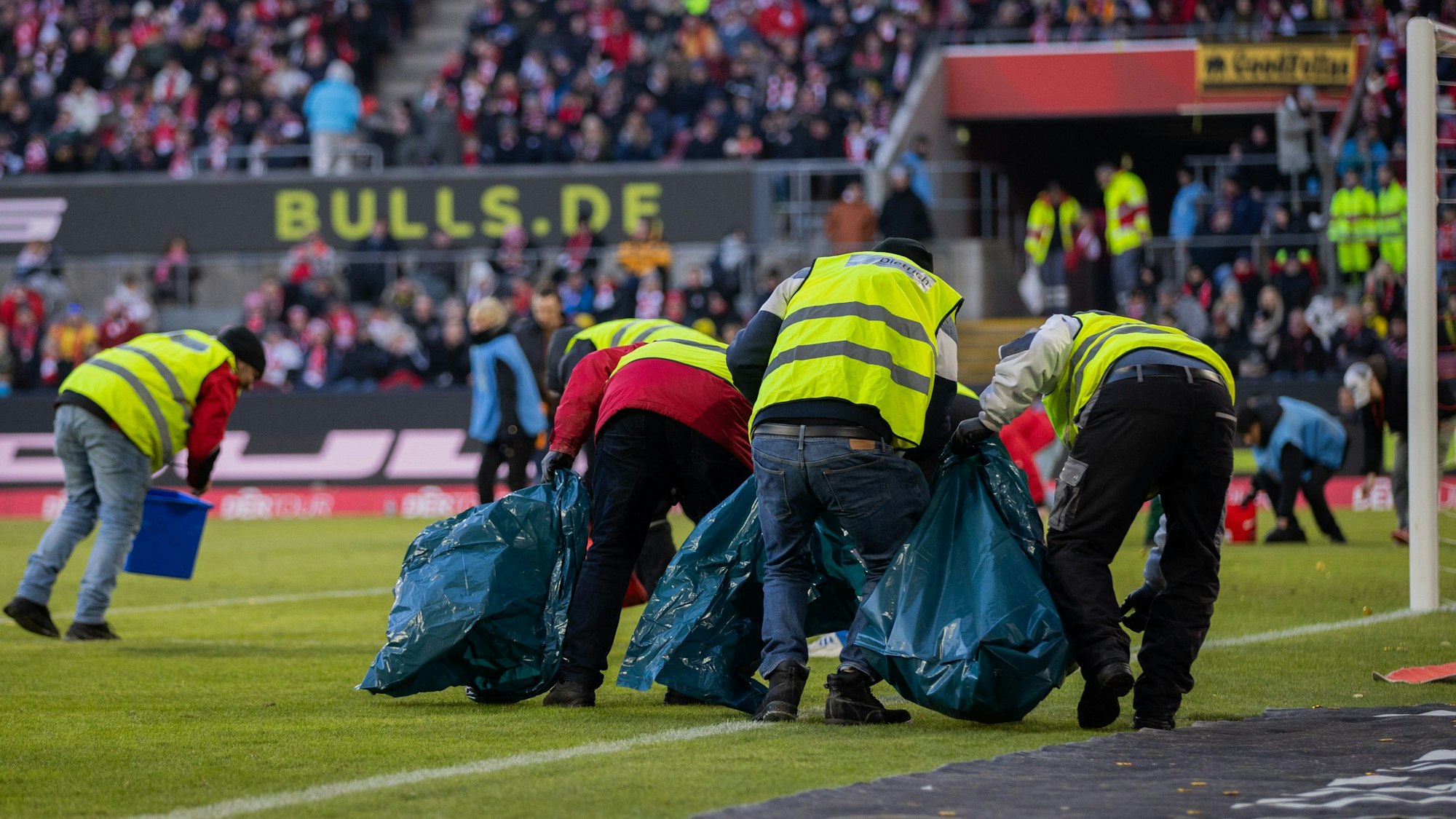 Ordner sammeln im RheinEnergie-Stadion Taler ein, die Fans auf das Spielfeld geschmissen haben.